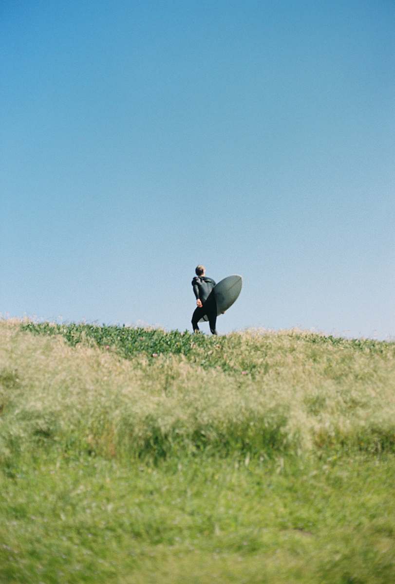 san francisco man standing on green grass mountain holding long surfboard ocean beach